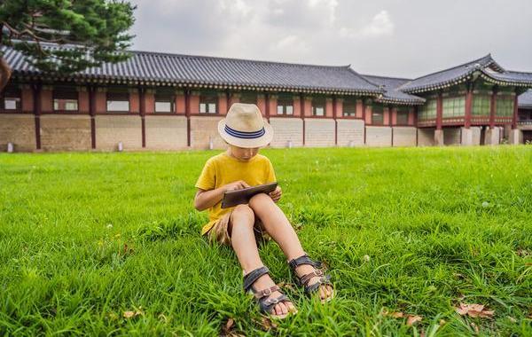 Young teen sitting on the grass using a tablet.