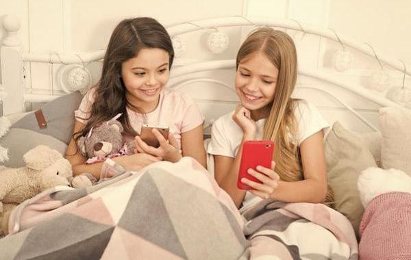 Two teens sitting together looking at their phones and smiling.