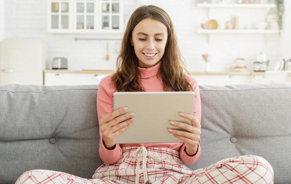 Teenager sitting on a couch with a tablet.