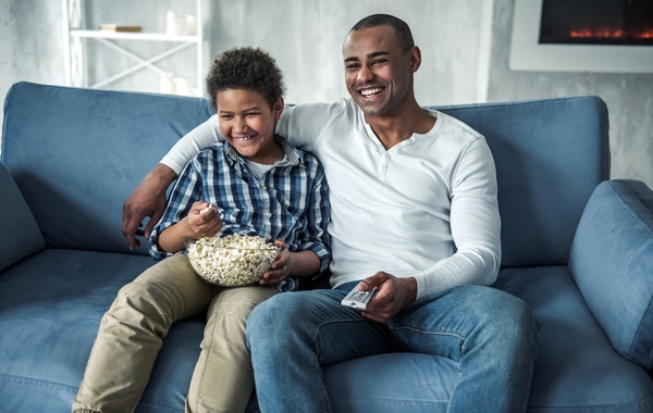 Father and son watching tv together while eating popcorn.