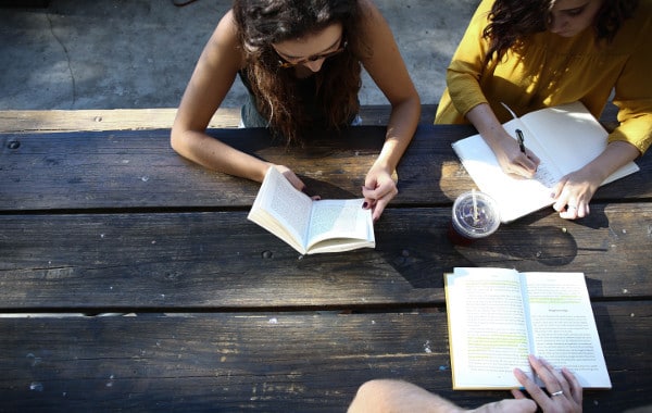 Teenage girls at an outside table reading.