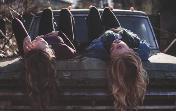 Two girls lying upside down on a couch side by side.