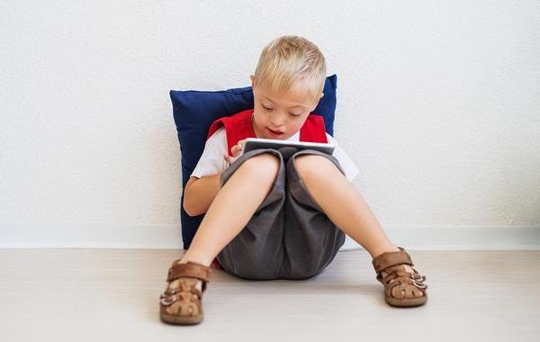 Teenage boy sitting against the wall typing on a tablet.