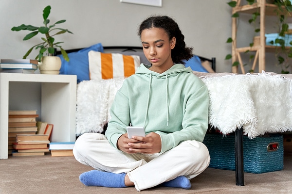 Teen sitting on the floor looking at her phone.