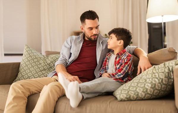 Father and son sitting on a couch having a discussion.