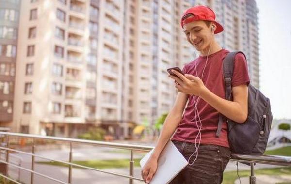 Teenage boy leaning against a railing while looking at his phone.
