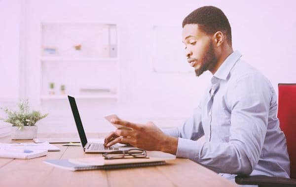 Man working on a laptop while using his phone.