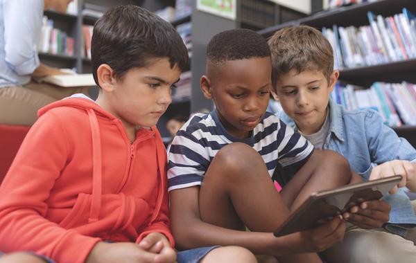Three kids sitting on the floor together looking at an iPad.