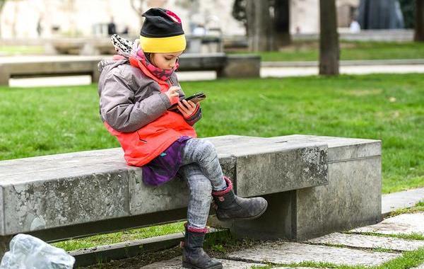 Child sitting on a concrete bench outside looking at her phone.