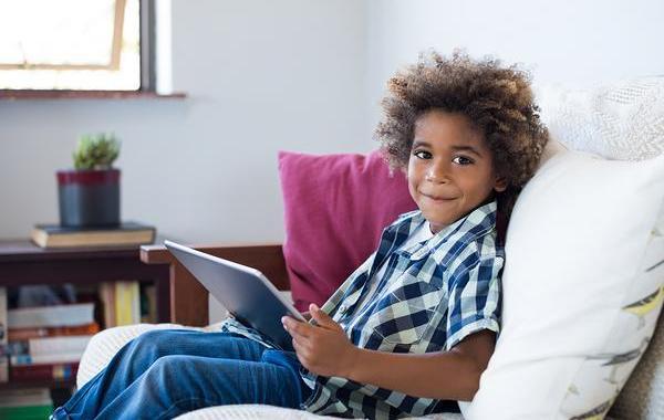 Young teen sitting on a couch smiling while holding a tablet.