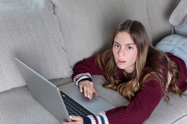 Teen lying on a couch looking at her laptop.